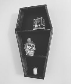 a black and white photo of a shelf with a skull head on the top, candle holder in the middle