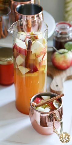 a pitcher of apple cider next to a glass full of apples and cinnamon sticks