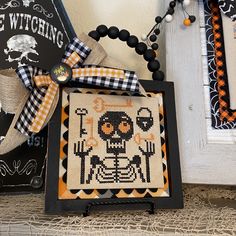 a cross - stitch halloween decoration is displayed on a shelf next to other items and decorations