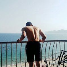 a man standing on top of a balcony next to the ocean with his back to the camera