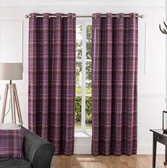 a living room filled with furniture and a window covered in purple plaid drapes next to a chair