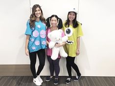 three young women standing next to each other in front of a wall holding stuffed animals