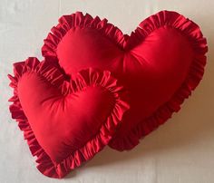 two red heart shaped pillows sitting on top of a white sheet