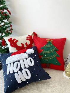 three christmas pillows sitting on top of a bed next to a christmas tree and other decorations