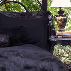 a bed with black sheets and pillows in front of a lamp on a night stand