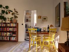 two yellow chairs sitting at a table in front of a bookshelf filled with books