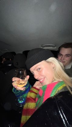 a woman holding a wine glass in her hand while sitting next to two men on the back of a car