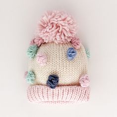 a knitted hat with pom - poms on the top and bottom, sitting on a white surface