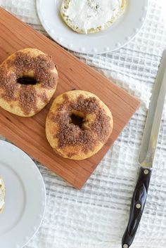 two donuts sitting on top of a cutting board next to a knife and fork