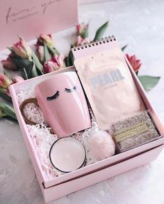 a pink box containing a coffee mug, candle and other items with flowers in the background