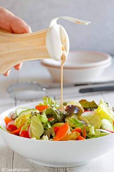 someone pouring dressing on a salad in a white bowl