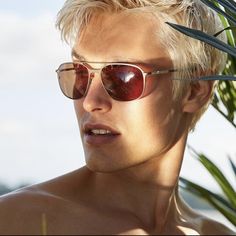 a young man wearing sunglasses standing next to a palm tree and looking off into the distance