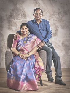 a man and woman are sitting on a chair posing for a photo in front of a gray background