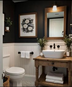 a white toilet sitting next to a sink in a bathroom under a framed painting on the wall