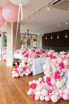 pink and white flowers are arranged on the floor in front of tables with large balloons