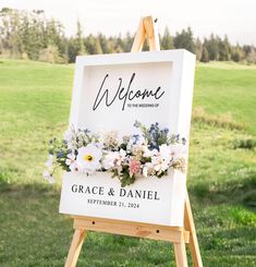 a welcome sign with flowers on it in front of a green field and grass area