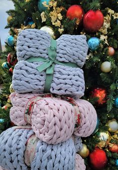 a pile of knitted blankets sitting next to a christmas tree with ornaments on it