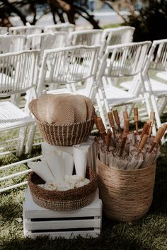 an outdoor ceremony with white chairs and wicker baskets filled with napkins, paper towels and straw hats