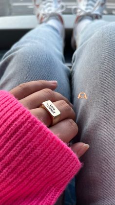 a person wearing a pink sweater and holding a gold ring with the word love written on it