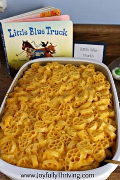 a casserole dish filled with macaroni and cheese next to a little blue truck book