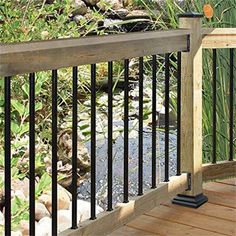 a wooden deck with black iron railings next to a small stream in the woods