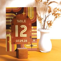 a table number card next to a vase with dried flowers