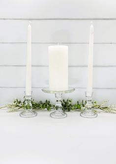 three candles sitting on top of a table with greenery