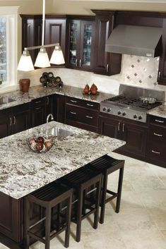 a large kitchen with marble counter tops and dark wood cabinets, along with an island in the middle