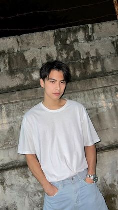 a young man standing in front of a stone wall with his hands in his pockets