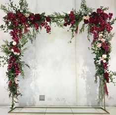 an arrangement of flowers and greenery in front of a white wall