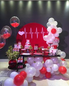 a table topped with lots of balloons next to a red heart balloon wall and heartbeat sign