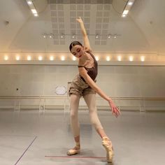 a young ballerina is practicing her moves in an empty room with lights on the ceiling