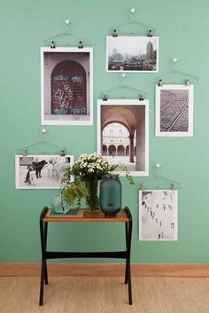 a green wall with pictures hanging on it and a vase full of flowers in front