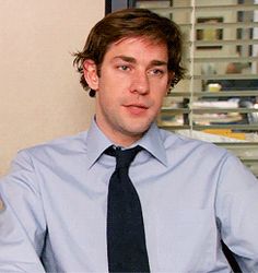 a man wearing a blue shirt and black tie sitting in front of a computer monitor