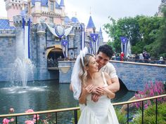 a bride and groom standing in front of the castle at disneyland world with their arms around each other