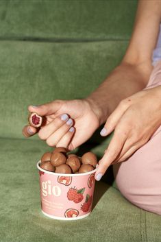 a woman sitting on a green couch holding a cup filled with nuts