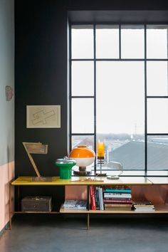 a table with books and a lamp on it in front of a window that looks out onto the city