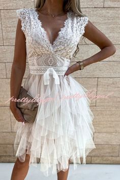 a woman wearing a white dress with sheer lace on the top and bottom, standing in front of a brick wall