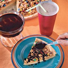 a piece of pizza on a blue plate next to a cup of coffee and a drink