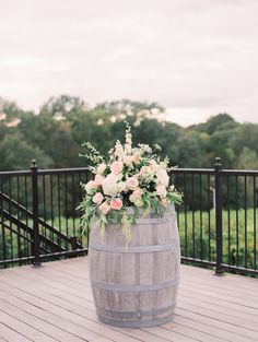 a wooden barrel with flowers in it sitting on a deck next to a black railing