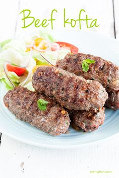 some meat on a plate with salad and lettuce in the background that says beef kofta