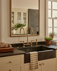 a bathroom sink sitting under a large mirror next to a window with potted plants on it