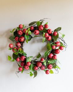 a wreath with red apples and green leaves hanging on the wall next to a white wall