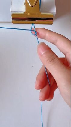 a hand is holding a piece of blue string with a golden object on top of it