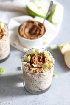 two glasses filled with oatmeal sitting on top of a table next to an apple