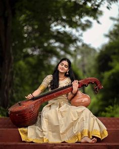 a woman sitting on top of a wooden bench holding a musical instrument