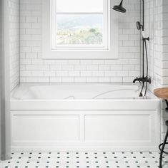 a white bathroom with black and white tile flooring is shown in this image, there is a window above the bathtub