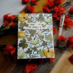 a card with pumpkins and leaves on it sitting next to some red flower petals