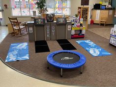 an indoor gym area with blue and black trampolies on the floor, rugs in front of windows