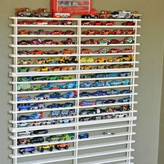 a white rack filled with lots of toy cars on top of a wall next to a window